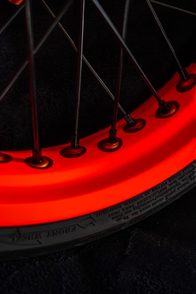 Détail du vinyle rouge GXS sur le rebord de jante supermotard, rayons et pneu visibles